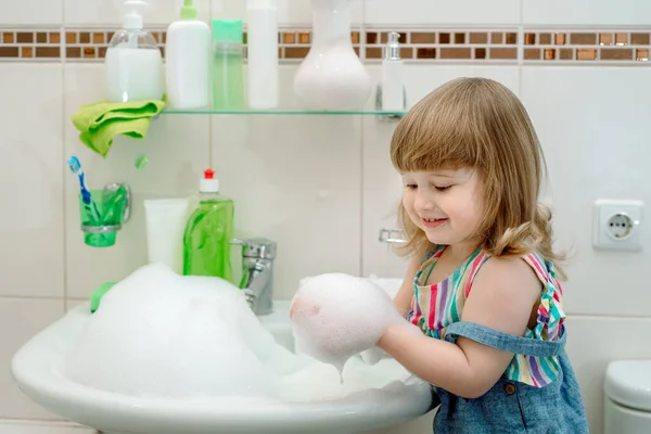 Ванная пена baby.Cleaning ванной комнате. Пена в раковине, зеленое мыло и зеленые перчатки в девушке. Чистый дом. Уборка. ребенок моет водопровод. — стоковое фото