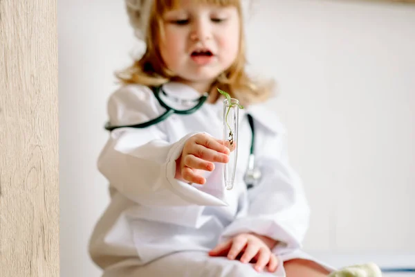 Bébé fille sous la forme d'un médecin joue avec un tube à essai. Laboratoire de recherche. Germe in vitro. — Photo