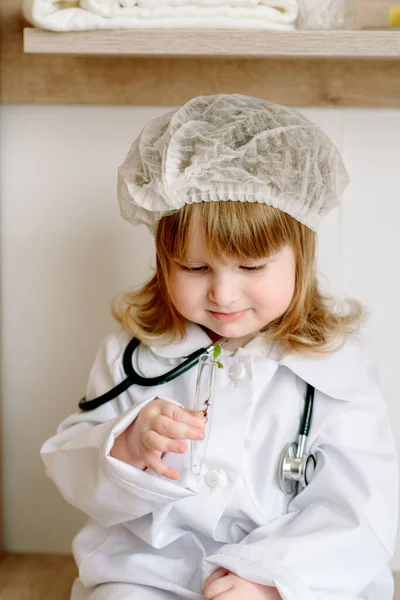 La bambina sotto forma di medico gioca con una provetta. Laboratorio di ricerca. Germoglio in vitro. — Foto Stock