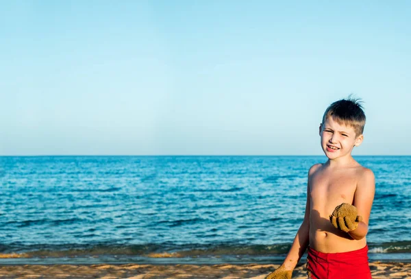 Vacaciones marítimas. Lindo chico en la playa juega con la arena. Funde un castillo de arena y pasteles. puesta del sol, cielo azul y relajarse espacio concept.copy viaje — Foto de Stock