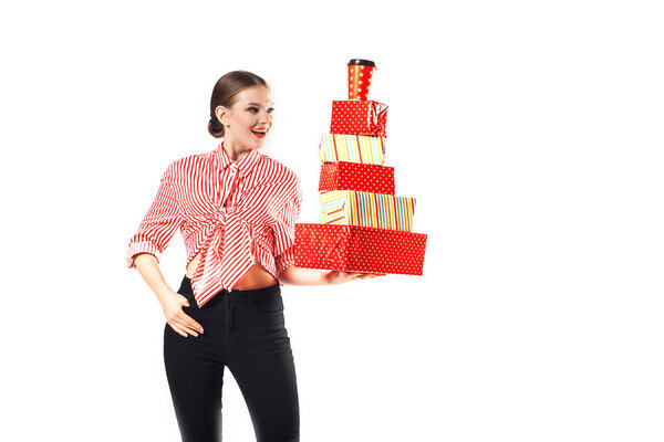 Молодая женщина держит подарочную коробку. Улыбающаяся счастливая девушка на белом фоне. Много красных коробок. Девушка на вечеринке, дне рождения или валентинки.