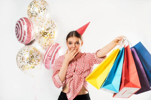 Fröhliches Mädchen, Party. Herrliche schlanke junge Frau trägt ein gestreiftes rotes Hemd und hat Spaß, bunte Taschen mit Geschenken. auf weißem Hintergrund im Atelier — Stockfoto