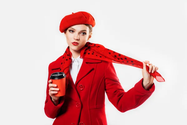 Mladá krásná módní žena ve stylovém zimním červeném kabátě, hedvábný šátek, červený baret na bílém ve studiu. Kopírovat prostor Milující Valentýna. Drží kávu v rukách.Cestovní koncept — Stock fotografie