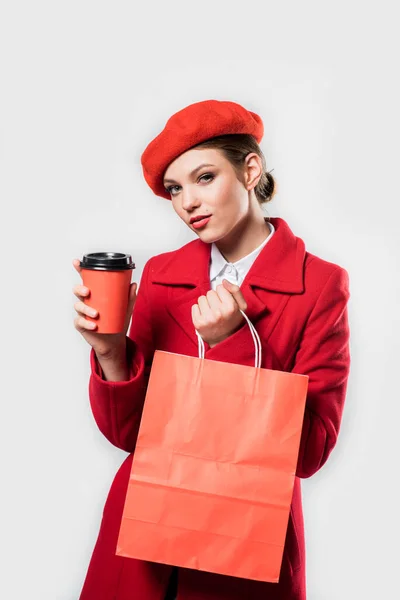 Vertikales Porträt junge schöne modische Frau trägt stilvolle Winter roten Mantel, Seidenschal, rote Baskenmütze auf einem weißen in Studio.Loving Valentines Day.Papiertasche in den Händen. Konzept des Verkaufs und Einkaufs — Stockfoto