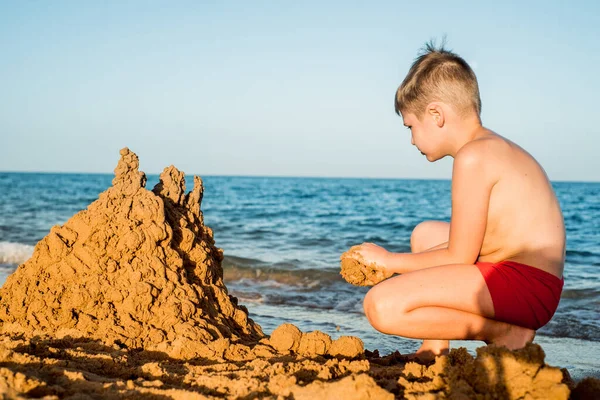 Castelo de areia feito de areia pelas mãos de uma criança na costa.Mar ao pôr do sol, areia branca na praia.Sol por do sol, luz amarela Imagens De Bancos De Imagens Sem Royalties