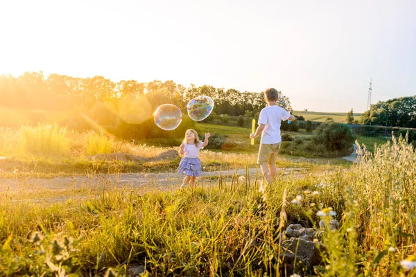 Crianças felizes brincando com bolhas de sabão em uma natureza de verão. Bolhas no pôr do sol — Fotografia de Stock