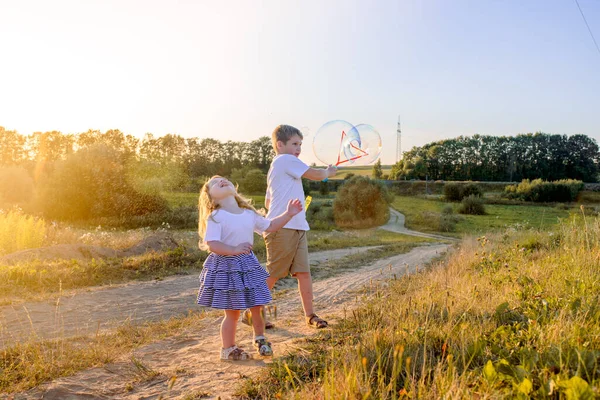 Glückliche Kinder, die im Sommer mit Seifenblasen spielen. Blasen im Sonnenuntergang — Stockfoto