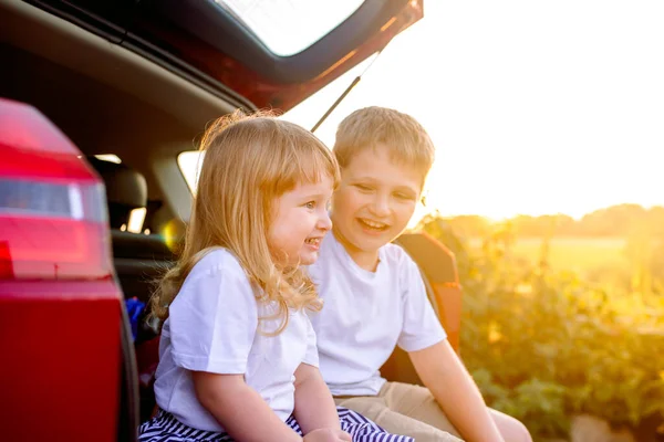 Deux petits enfants jettent un coup d'œil hors de la voiture au coucher du soleil.. — Photo