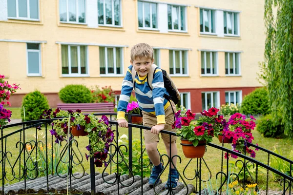 Szczęśliwy chłopak na szkolnym podwórku. Mały chłopiec z książkami i plecakiem. Dziecko na świeżym powietrzu w ciepły słoneczny dzień, Powrót do szkoły . — Zdjęcie stockowe