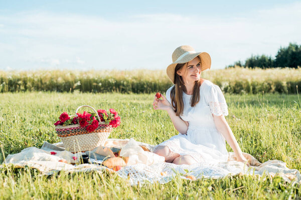 Field in daisies, a bouquet of flowers.French style romantic picnic setting. Woman in cotton dress and hat , strawberries, croissants, flowers on blanket, top view. Outdoor gathering concept