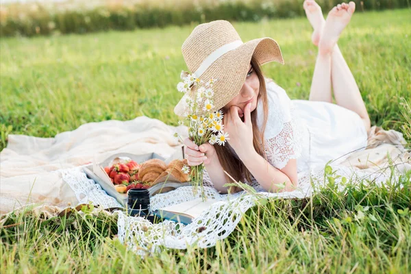 小女孩在田野里和雏菊在一起，夏天在村子里。年轻的微笑的女人在户外放松，野餐，躺在草地上的毛毯上 — 图库照片