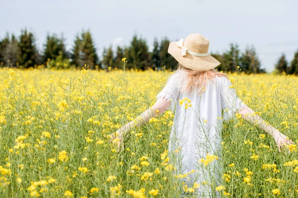 Portrait d'une jolie fille heureuse dans un champ de blé d'été, en robe blanche et chapeau.Fleurs de colza jaunes. ensoleillé journée d'été en plein air — Photo