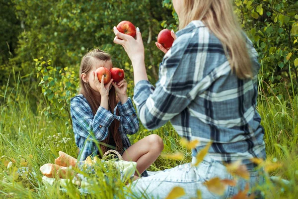 Happy smiling woman and fun enjoying kid, mother holding the red apples near the eyes.Picnic in the park, happy family. Sunny summer day outdoors — Stock Photo, Image