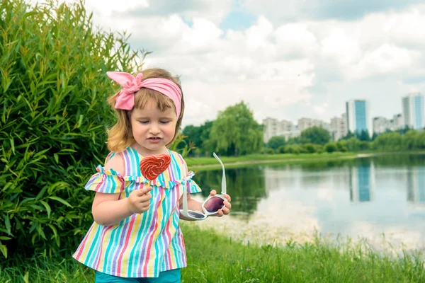 Lustig mit schmutzigen Lippen.Mädchen mit einem Lutscher in einer Großstadt, einer Metropole. Eine glückliche Kindheit, ein süßes Leben. Sommerlicher Lebensstil. Modisches Mädchen. — Stockfoto