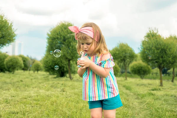 Pequeña niña hermosa soplando burbujas de jabón en el parque de la ciudad Ureki. Ecología y Naturaleza al aire libre. Verano caluroso y soleado. feliz infancia, estilo de vida — Foto de Stock