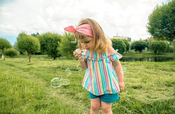 Pequena menina bonita soprando bolhas de sabão no parque da cidade Ureki. Ecologia e Natureza ao ar livre. Verão quente ensolarado. infância feliz, estilo de vida — Fotografia de Stock