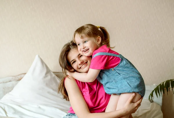 Niños felices divirtiéndose con almohadas en la cama.niños juegan en el dormitorio. dos hermanas. adolescente y niña risa, abrazo y beso. — Foto de Stock