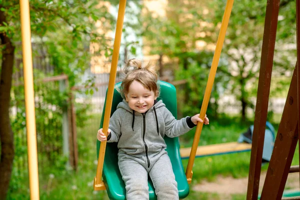 Сміється дитина на гойдалках в літньому парку. грає в дитячі ігри, бігає і стрибає. безтурботне дитинство . — стокове фото