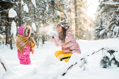Anne ve kızı karlı bir kış ormanında eşarba sarılı..