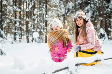 Anne ve kızı karlı bir kış ormanında eşarba sarılı..