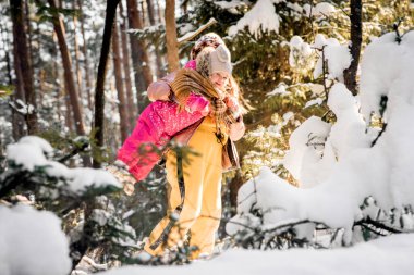 Anne ve kızı karlı bir kış ormanında eşarba sarılı..