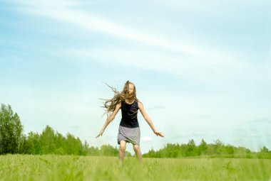 Baharda çimlere atlayan kız çocuğu. Saha, ufuk ve gökyüzü. Mutlu çocukluk ve özgürlük. Açık havada yaşam tarzı..