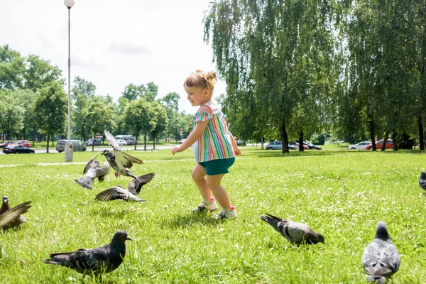 Uma menina corre para pombos. Baby Girl Chasing Pigeons In Outdoors City Park. infância feliz alegre, corre rindo e gritando. — Fotografia de Stock