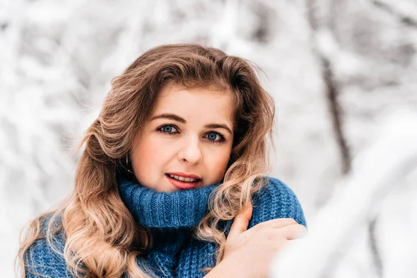 beautiful winter woman in a blue cozy knitted sweater playing with snow