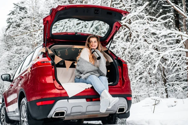 winter romance concept car travel in winter, in red car drinks hot tea from a thermos, picnic in a frosty winter forest