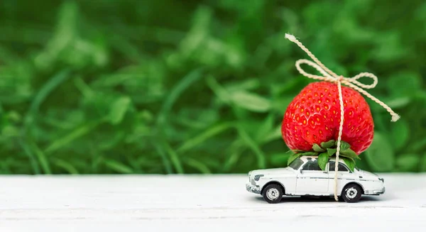 on a green background a small toy car with red strawberries place inscription. Concept summer is coming