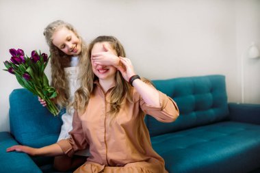 Evinde annesini selamlayan tatlı küçük bir kız. Mor lale buketi. Anneler Günü konsepti