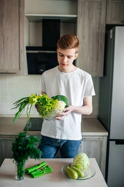 Comida sana y fresca. Hombre joven vegetariano está cocinando ensalada en la cocina interior — Foto de Stock