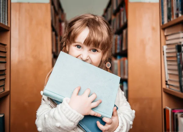 Дитяча дівчинка в бібліотеці з книгами в руках. милий малюк досліджує книжкові полиці — стокове фото