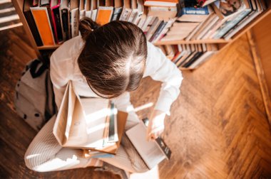 Eğitim, lise, üniversite, öğrenim konsepti - kütüphanede kitap okuyan gülümseyen kız öğrenci