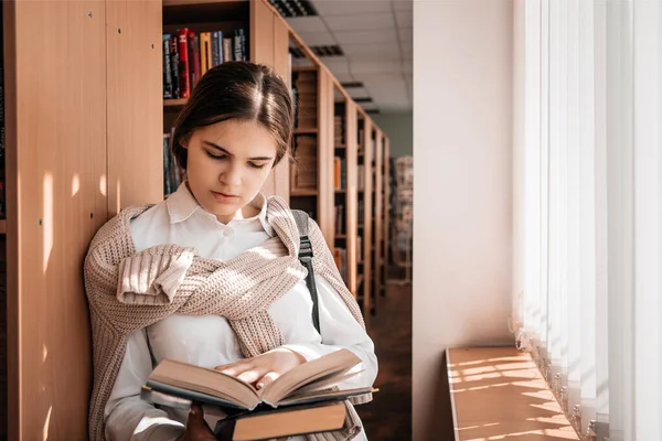 Освіта, середня школа, університет, концепція навчання - усміхнена студентка читає книгу в бібліотеці — стокове фото