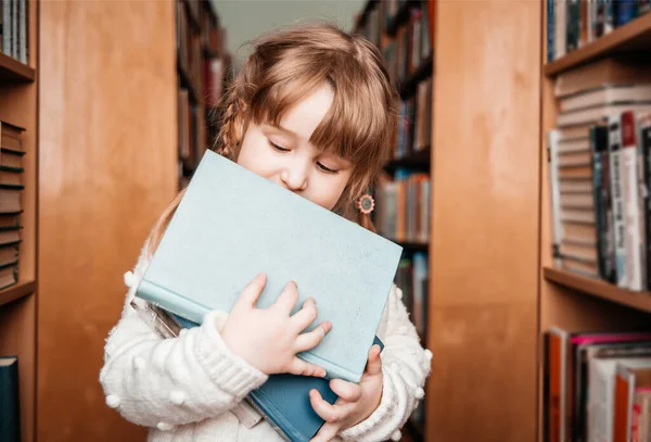 Дитяча дівчинка в бібліотеці з книгами в руках. милий малюк досліджує книжкові полиці — стокове фото