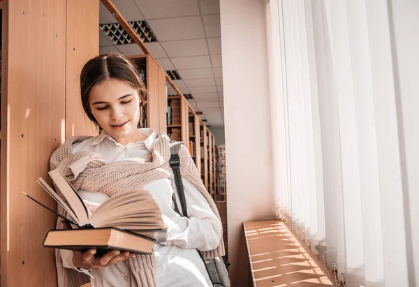 Освіта, середня школа, університет, концепція навчання - усміхнена студентка читає книгу в бібліотеці — стокове фото