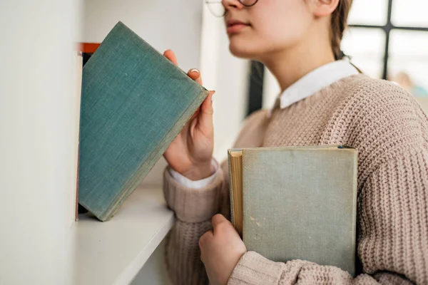 Молода дівчина стоїть біля книжкової полиці в бібліотеці — стокове фото