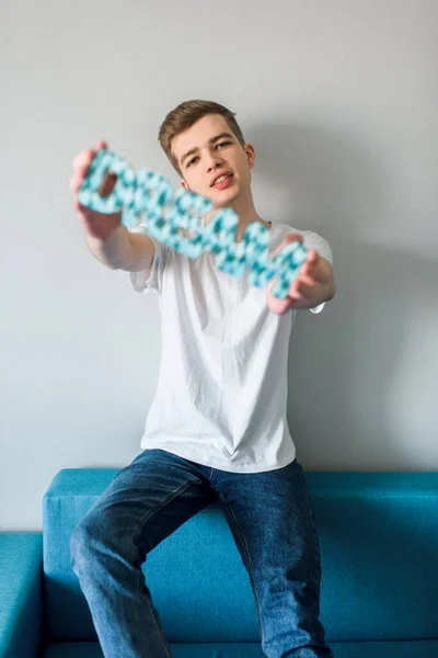 Um tipo sorridente e sonhador, um jovem deitado no sofá azul em casa. nas mãos da inscrição a palavra sonho — Fotografia de Stock