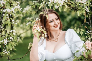 Güzel sarışın kadın elma ağacının yanında duruyor.