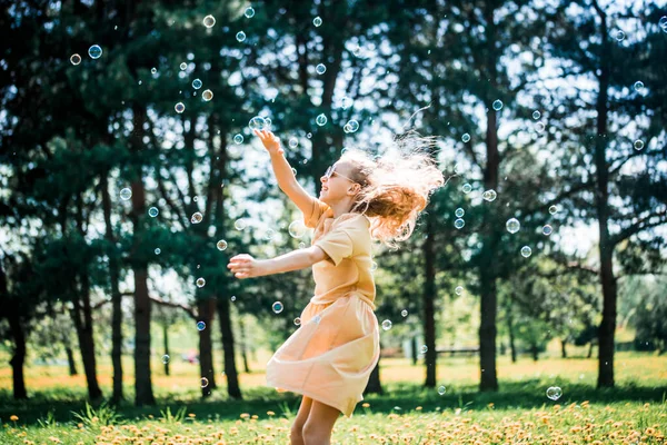 小女孩在大自然中玩耍。跳着跑着追着肥皂泡，在公园里过着积极的生活 — 图库照片