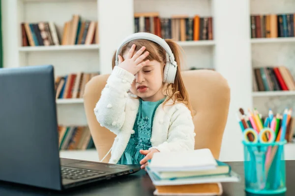 Emocional caucasiano menina de quatro anos fazendo lição de casa usando o caderno para o ensino à distância sentado à mesa. Conceito de aprendizagem online à distância. Fotos De Bancos De Imagens