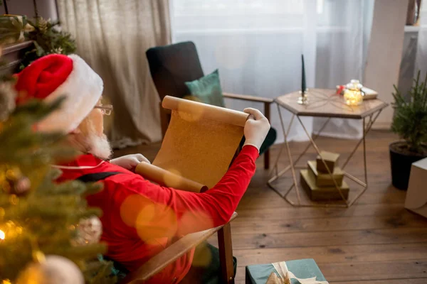 Mikołaj w domu czyta listy i listy życzeń dzieci. Ozdobiona choinka ze światłami. Prezenty i niespodzianka na Nowy Rok. — Zdjęcie stockowe