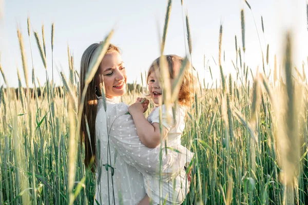 Família feliz, mãe em um vestido com um bebê pequeno bonito em um campo de trigo dourado ao pôr do sol. dia de verão — Fotografia de Stock