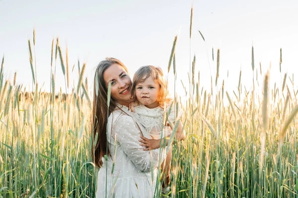 Família feliz, mãe em um vestido com um bebê pequeno bonito em um campo de trigo dourado ao pôr do sol. dia de verão — Fotografia de Stock