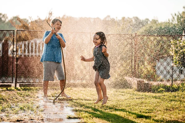 暑い夏の日に庭のホースで遊んでいる小さな子供たち — ストック写真