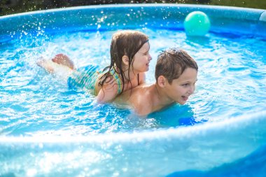 Çocuklar sıcak yaz mevsiminde havuzda bir topla oynarlar. Kız ve erkek açık havada