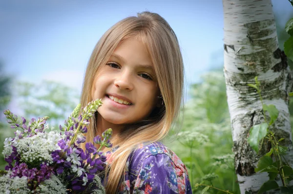 Menina rindo bonita em um campo de flores roxas de tremoço . — Fotografia de Stock