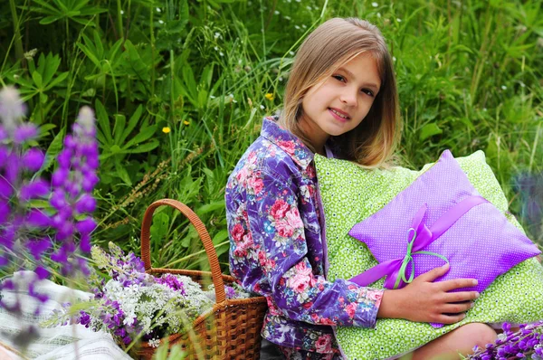 Family picnic. Basket with flowers and next to a beautiful little girl with cushions — Stok fotoğraf