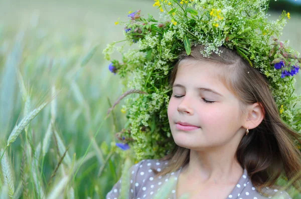 Menina sorridente feliz com os olhos fechados no campo nos ouvidos. Grinalda floral na cabeça — Fotografia de Stock